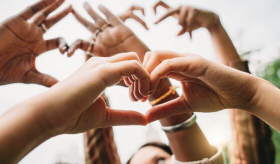 People hold up their hands with heart signs.
