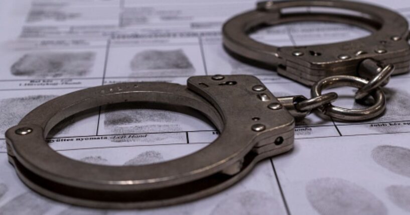 A pair of handcuffs sit on top of a fingerprinting chart in a dimly lit room.