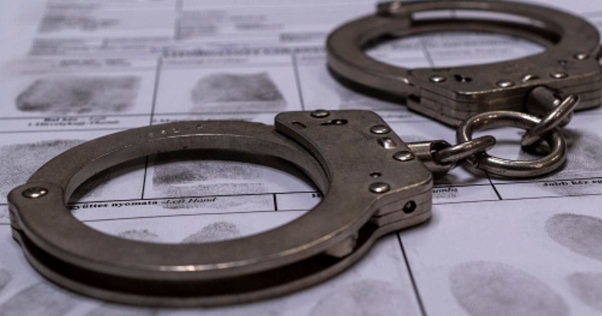 A pair of handcuffs sit on top of a fingerprinting chart in a dimly lit room.