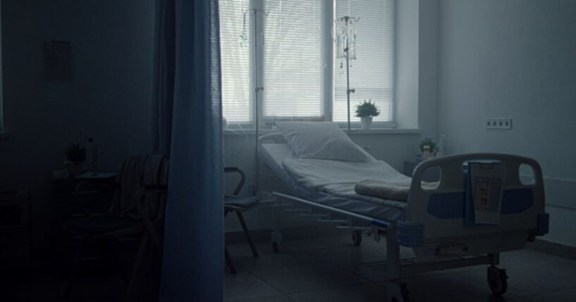 A hospital bed sits empty in a corner.