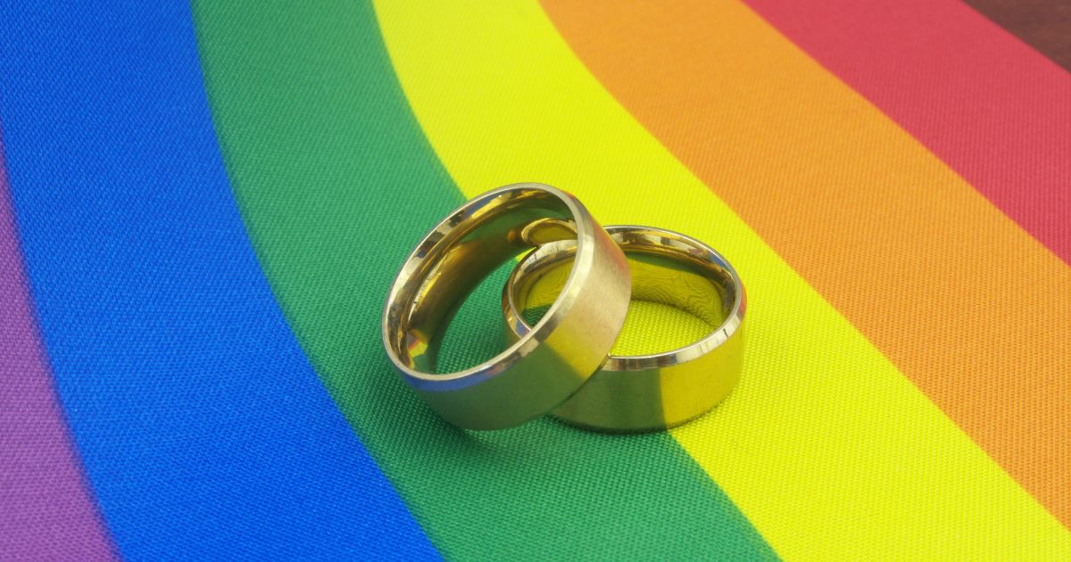 Gold wedding rings sit on top of an LGBT pride flag.