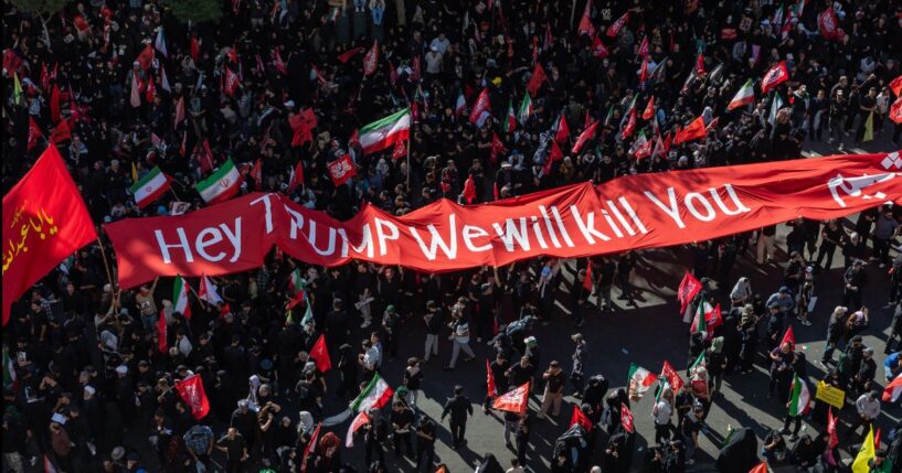Mourners of the authoritarian Iranian Supreme Leader Ayatollah Ali Khamenei hold up a banner threatening the life of President Donald Trump on July 9, 2026 during a funeral procession for the leader in Mashhad, Iran.