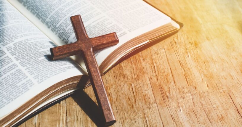 A close-up image of a Christian cross necklace lying against an open Bible.