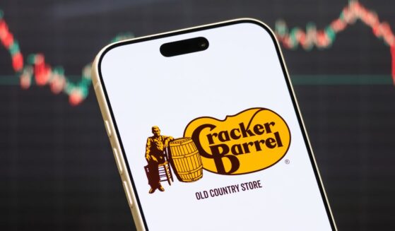 A Cracker Barrel logo displayed on a phone in front of a stock market chart.