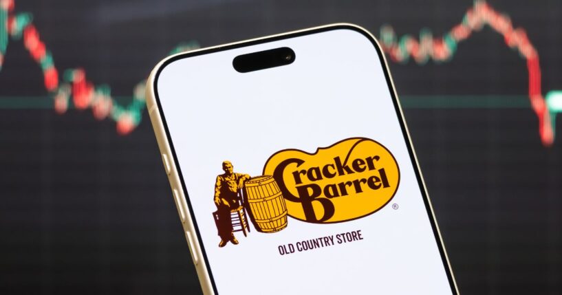 A Cracker Barrel logo displayed on a phone in front of a stock market chart.