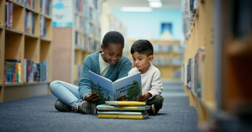 Children sit on the floor of a library as they read fairy tale books together.