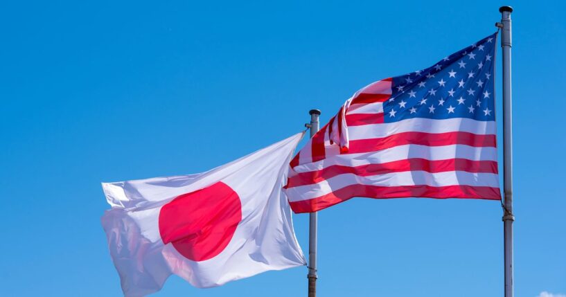 American and Japanese flags waving against a blue sky.
