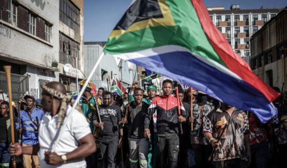 Protesters hold sticks and flags while chanting slogans as they march during a demonstration by the "March & March" and Operation Dudula movements marking an unofficial deadline set by citizen-led groups for undocumented foreign nationals to leave South Africa, in Johannesburg, on June 30, 2026.
