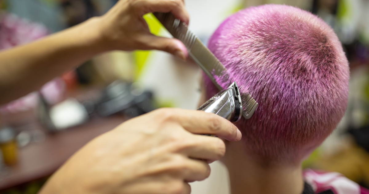 A female hairdresser giving a hairstyle to a young woman with pink dyed short hair.