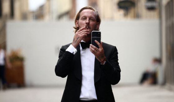 British actor Laurence Fox gestures with his phone, live-streaming, as he stands behind security barriers after arriving to attend a speech by British far-right activist Tommy Robinson to The Oxford Union, in Oxford, western England, on June 17, 2026.