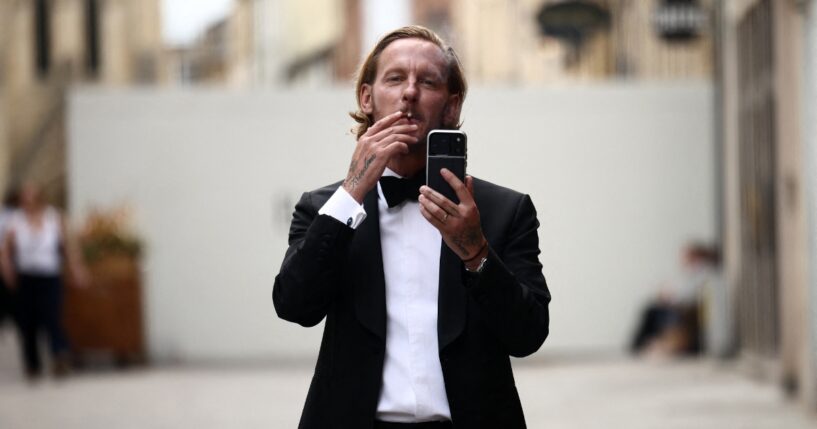 British actor Laurence Fox gestures with his phone, live-streaming, as he stands behind security barriers after arriving to attend a speech by British far-right activist Tommy Robinson to The Oxford Union, in Oxford, western England, on June 17, 2026.