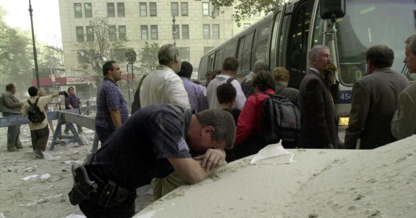 An exhausted police officer rests on a car covered in dust near the World Trade Center on Sept. 11, 2001, in New York as people board a bus to be evacuated after two hijacked planes crashed into the landmark towers.