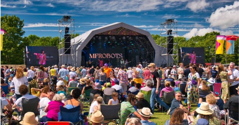 A large crowd in front of a stage at an outdoor summer music festival in England.