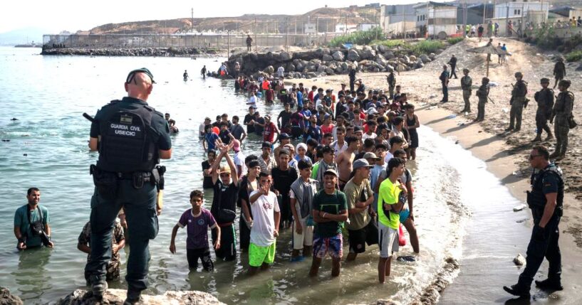 Members of the Guardia Civil USECIC guard migrants on Tarajal beach after they crossed the border between Spain and Morocco on July 31 in Ceuta, Spain.