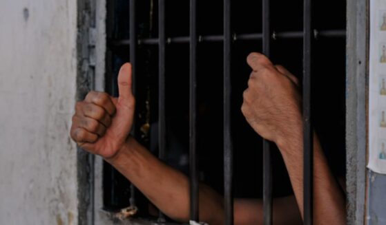 A prisoners hands are reaching from behind cell bars.
