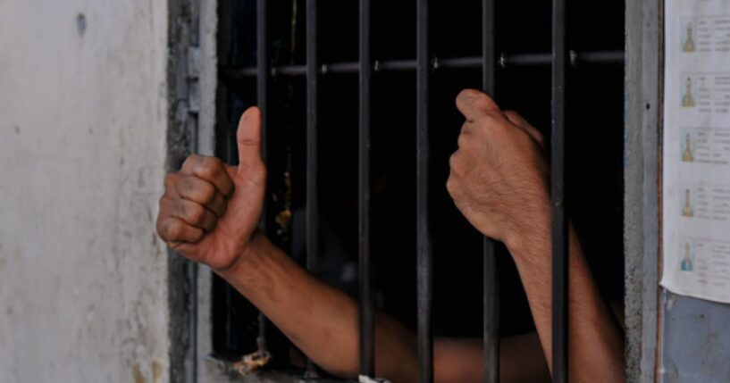 A prisoners hands are reaching from behind cell bars.