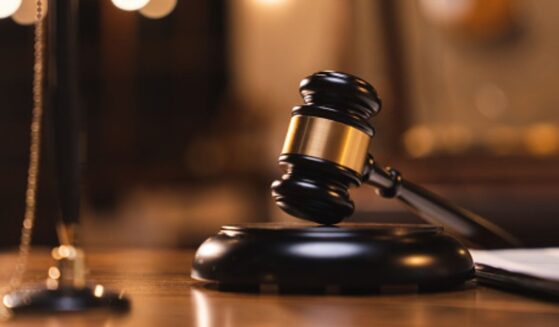 A gavel lays on a wooden block on a wooden table in a dimly lit room.
