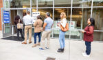 People stand in a line outside a polling center during the day.