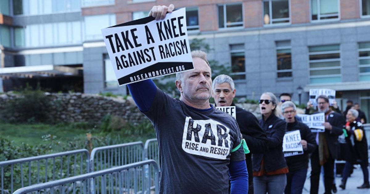 A man protesting racism with RAR stands holding a sign above his head leading a group of protesters outside the an NFL League Meeting on October 17, 2017 in New York City, NY.