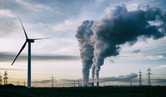 Plumes of smoke blow from a factory near a wind turbine.