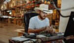 A man wearing a cowboy hat sits at a table and works.