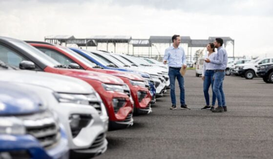 A young couple looks at cars on a car dealership lot.
