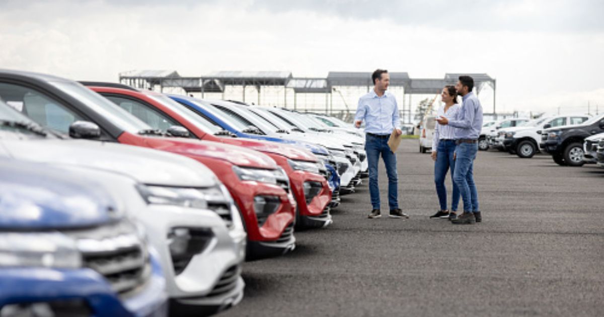 A young couple looks at cars on a car dealership lot.