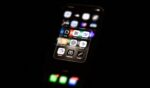 A phone screens displays AI apps on their user interface in a dark space.