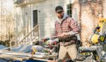A man works in the yard of a house with wood and tools.