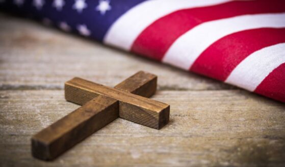 A cross and an American flag sit next to each other on a wooden table.