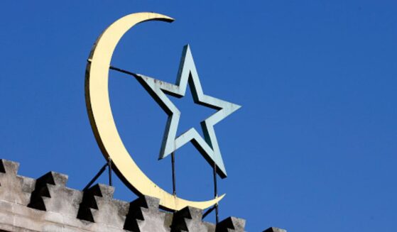 A crescent moon and star symbol is pictured on top of a building in the daylight.