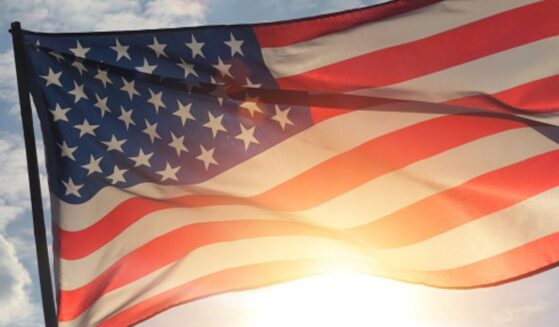 An American flag flies as the sun shines behind it.