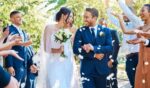 A couple gets married outdoors as attendees throw flower petals on them.