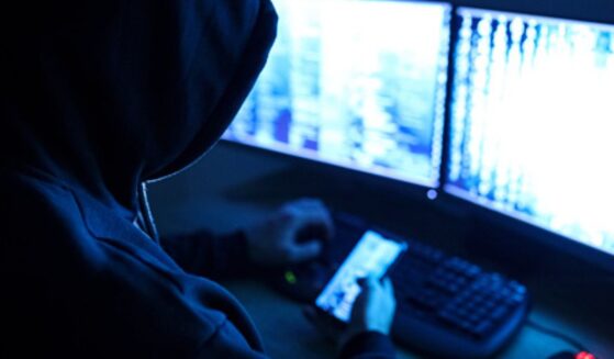A hacker works on a computer and phone.