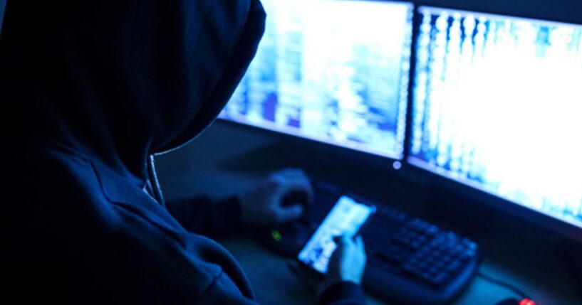 A hacker works on a computer and phone.