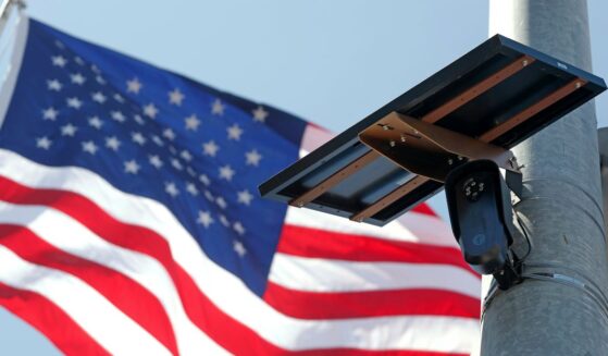 A Flock Safety camera is shown mounted in front of an American flag.