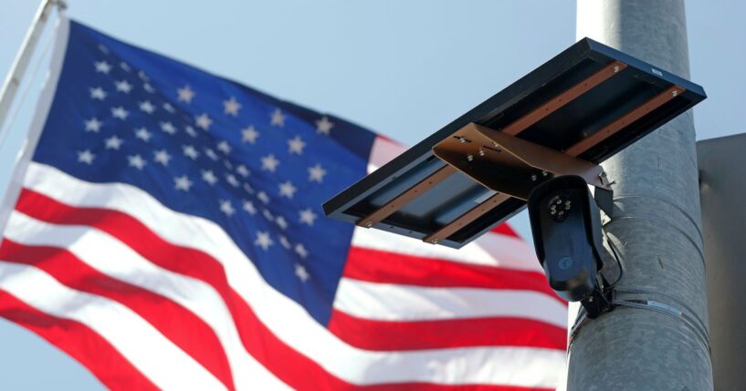 A Flock Safety camera is shown mounted in front of an American flag.