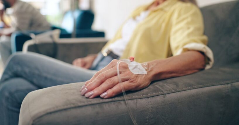 A cancer patient sits in a chair with an IV drip hooked up to her hand.