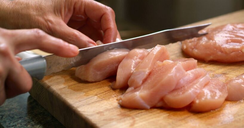 A close-up shot of a woman cutting raw chicken.