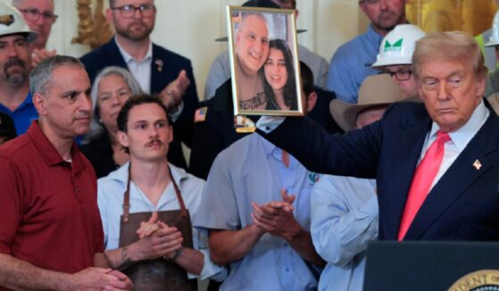 Joe Abraham, left, in red shirt, watches as President Donald Trump holds up a photograph of Abraham and his daughter, Katie Braham, during an event in the East Room of the White House in June 2025.