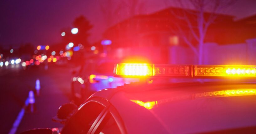 A police car at night alongside a road with emergency lights flashing.