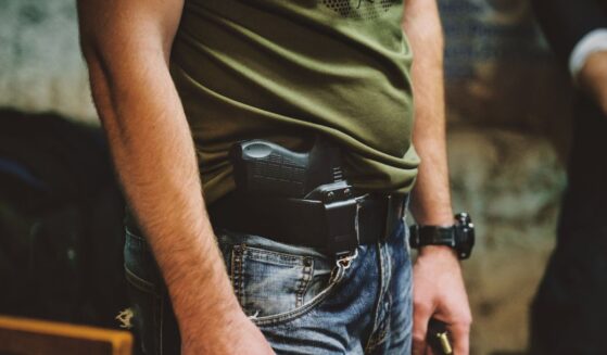 A person wearing jeans and a green shirt with a handgun holstered at their waist.