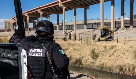 A Mexican National Guard soldier stands on the south side of the border as Texas National Guard troops place posts to extend a secondary fence at the U.S.-Mexico border on Jan. 7, 2023, as viewed from Ciudad Juarez, Mexico.