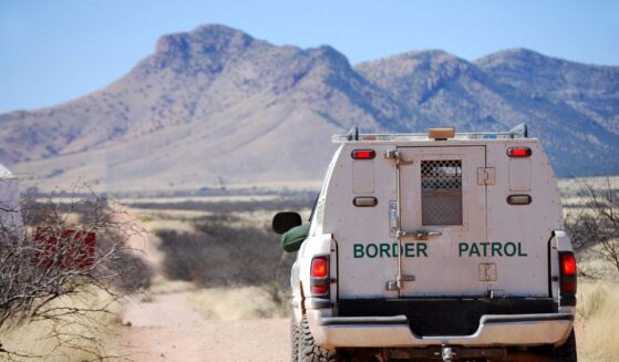 The back of a border patrol truck driving on a dirt road along the Mexican border in Arizona, with mountains in the background.