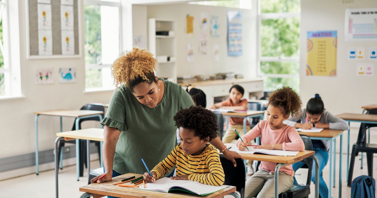 A teacher helps a child in an elementary school classroom.
