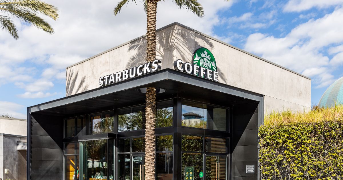A modern Starbucks Coffee building with a palm trees and a blue sky.