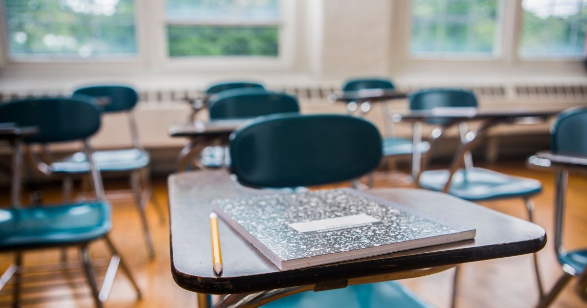A notebook and pencil on a desk in a school classroom.