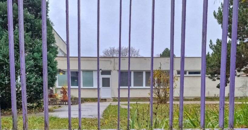 An empty school building behind a purple metal gate on a cloudy autumn day.