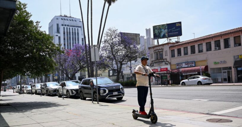 A pedestrian rides an electric scooter along Wilshire Boulevard in the Mid-Wilshire neighborhood on June 11, 2025, in Los Angeles, California.