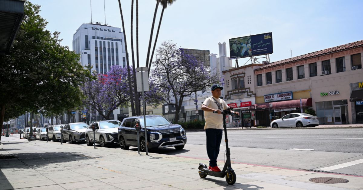 A pedestrian rides an electric scooter along Wilshire Boulevard in the Mid-Wilshire neighborhood on June 11, 2025, in Los Angeles, California.